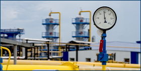 Photo of a yellow gas pipeline with additional equipment, pipes and a valve to shut off the gas supply. Against the background of blur is an image of gas compressor station