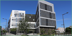 Een witgrijs gebouw van Coface met bomen en struiken ervoor, helderblauwe lucht op de achtergrond